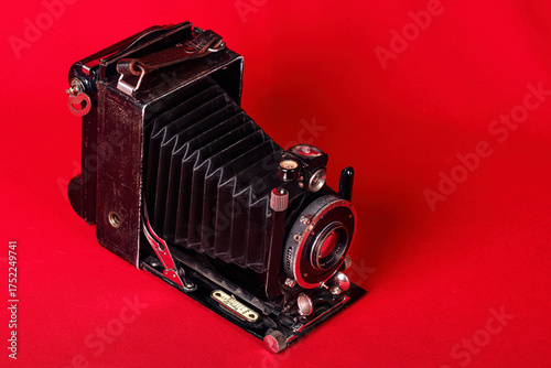 An old camera, with bellows, folding, portable on a red background.