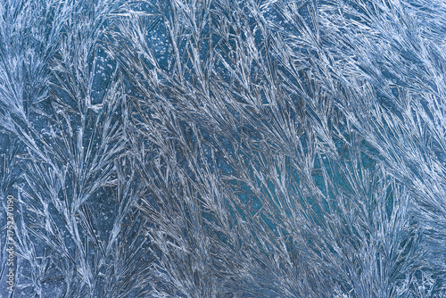 Close-up of blue frosty glass covered with sharp, sparkling ice crystal patterns. The composition showcases dense linear structures, rich texture and vivid contrast.