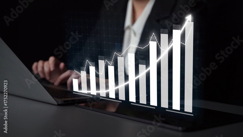Tableau sur toile A business professional works intently on a laptop, while a digital growth graph emerges, symbolizing analysis and strategic financial success in a modern workspace