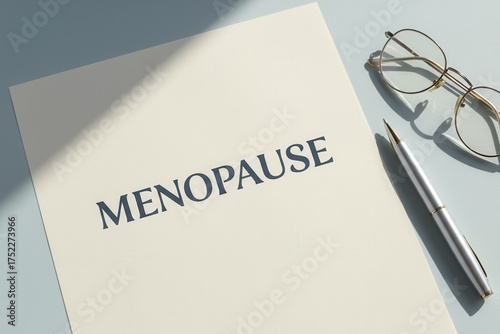The word menopause on a document with glasses and a pen. Women's health, aging, and hormonal change concept. Flat lay with copy space on a blue background