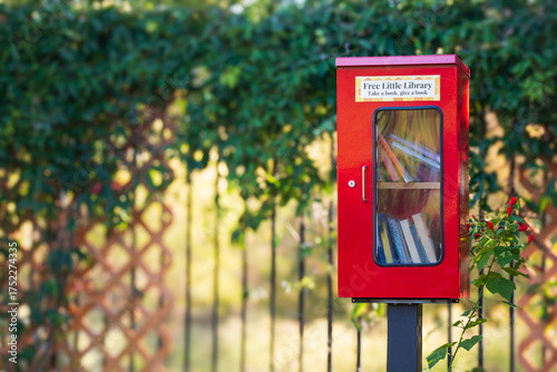 Red Little Free Library box in a quiet neighborhood park surrounded by beautiful nature 