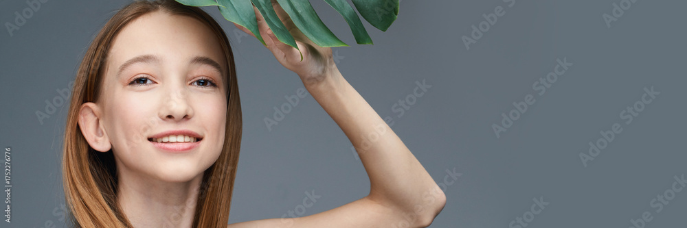 Obraz premium Young caucasian female holding leaf smiling against gray background with natural light.