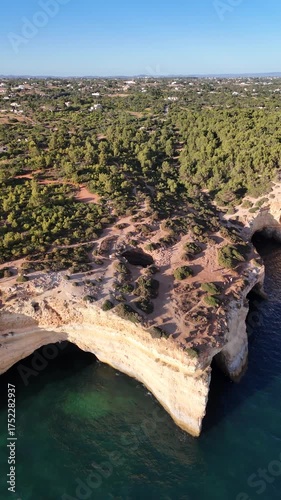 Aerial view of Benagil Cave from the sea with a large group of kayakers, boats, sailboat, and the cave roof hole visible along the Algarve coast in Portugal