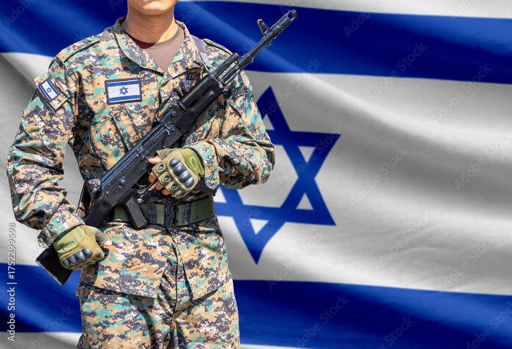 Obraz premium Israel flag with soldier in military uniform holding assault rifle in front of it