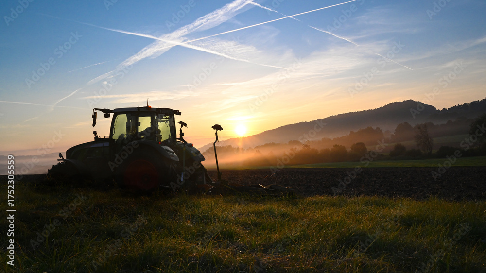 Fototapeta premium Tractor ploughing the field at sunrise morning in late summer or autumn landscape.