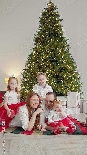 Joyful family gathers around beautifully decorated Christmas tree, sharing laughter and love. Children dressed in festive attire create memorable moments. Happy family having fun. Vertical. 4K, UHD
