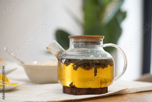 Brewing herbal tea in a glass teapot with a bamboo lid, resting on a wooden table, embodies a healthy lifestyle and wellness concept