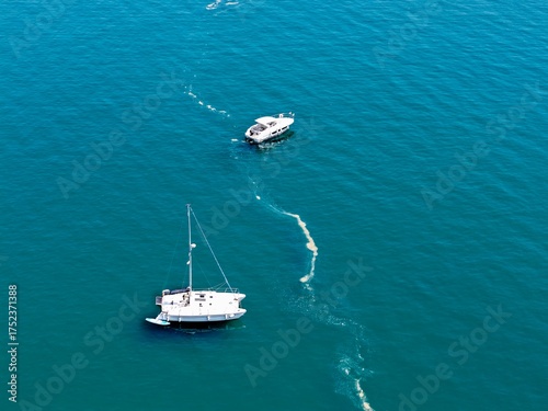 Aerial view of a small yacht and a sailboat sailing over the sea with turquoise water and shallow waves, luxury, lifestyle, ship, boat, cruise