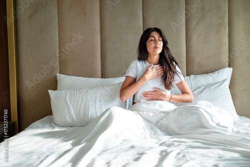 Relaxed woman sitting in the bed in the morning  and making breathing exercises 