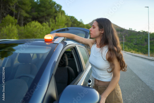 Girl stranded on a quiet roadside setting up an emergency light at sunset