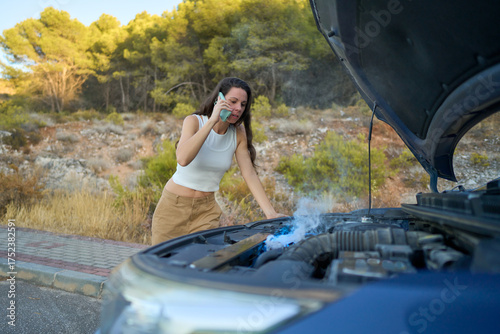 Girl stranded on the roadside as smoke rises from her broken-down car under the afternoon sun
