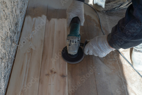 Wood floor sanding with electric sander by gloved worker in workshop