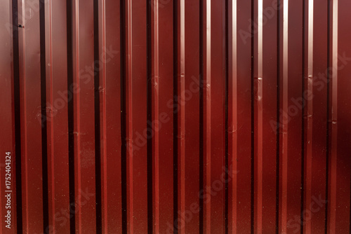 A close-up view of a red metal wall with vertical panels. The surface is smooth with a glossy finish, reflecting light subtly.