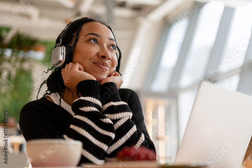 Young smiling African American woman student while listening to music in cafe using laptop