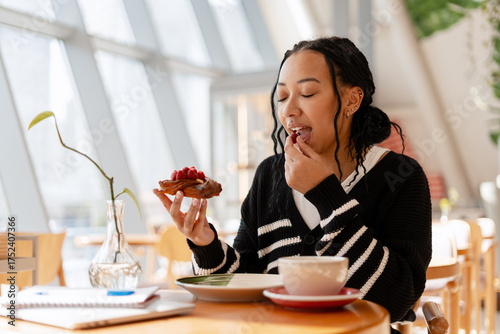 Canvas Print Young happy African American woman enjoying raspberry pastry and coffee break