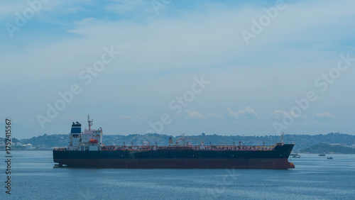 Large oil tanker anchored in calm blue waters. Coastal scene with distant land visible