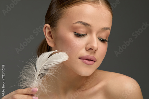 Woman applying smooth lotion to her face while holding a soft feather in a minimalist setting, emphasizing natural beauty and skin care techniques