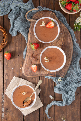 Wallpaper Mural Three white bowls of creamy chocolate mousse, one with a golden spoon, are elegantly arranged on a wooden board and table with fresh strawberries and delicate white flowers Torontodigital.ca