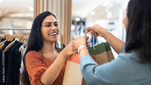 Fotografie Cheerful Indian customer taking shopping bags with clothes from associate