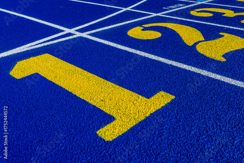 Close up photo of outdoor running track lane yellow number one, 1, on a new blue track with white lane lines.