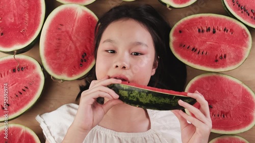 Portrait of a cheerful Asian young teenage girl eating many half pieces of fresh red watermelons, enjoying biting watermelon slices, healthy eating, abundant fruit, happiness, and hot summertime.