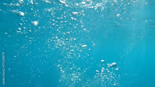 Dynamic air bubbles ascending in deep turquoise sea water.
