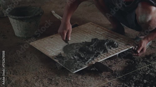 Professional construction workers prepare equipment and apply a thick layer of adhesive to the ceramic tiles to attach them to the walkway surface.