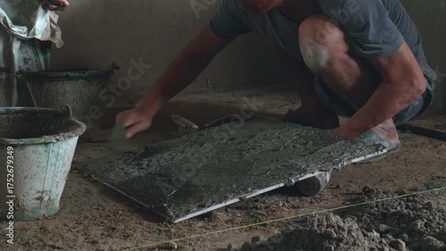 Professional construction workers prepare equipment and apply a thick layer of adhesive to the ceramic tiles to attach them to the walkway surface.