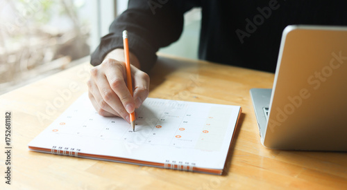 close up on businessman hand using pen to writing schedule on calendar to make appointment meeting or manage timetable each day at house for work from home concept