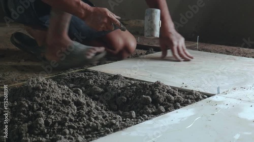 Professional construction workers prepare equipment and apply a thick layer of adhesive to the ceramic tiles to attach them to the walkway surface.