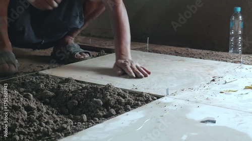 Professional construction workers prepare equipment and apply a thick layer of adhesive to the ceramic tiles to attach them to the walkway surface.