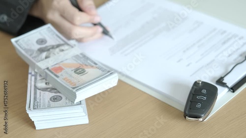 Car loan agreement signing with dollar bills and car key on wooden desk, concept of vehicle financing, auto loan, and car purchase deal.
