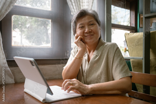 A cheerful elderly woman is happily using a tablet while sitting comfortably at her home