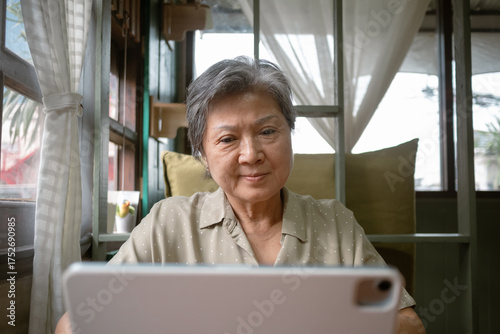 An elderly woman comfortably using a tablet in a cozy indoor setting filled with daylight