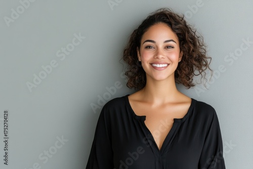 Smiling woman with curly hair in black shirt against gray backgr