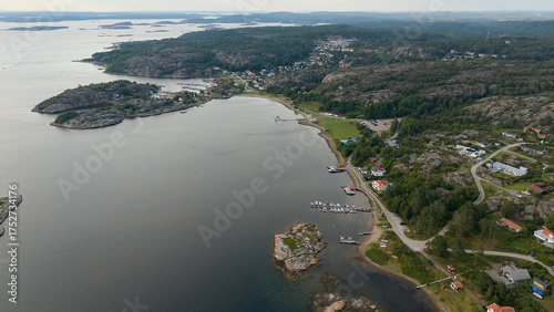 Aerial View of Coastal Village Near Strömstad, Sweden with Rocky Hills, Waterfront Homes, Small Harbor, and Calm Sea on an Overcast Day