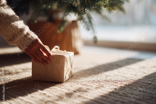Hand placing gift box under Christmas tree