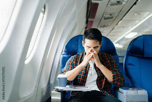 Travel stress, jet lag, or motion sickness. Young man with a headache or fatigue during a long flight. Tired passenger on a business trip.