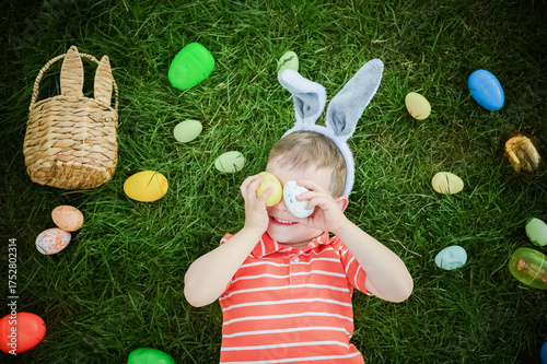 Happy Boy Playing with Easter Eggs on Grass Wearing Bunny Ears