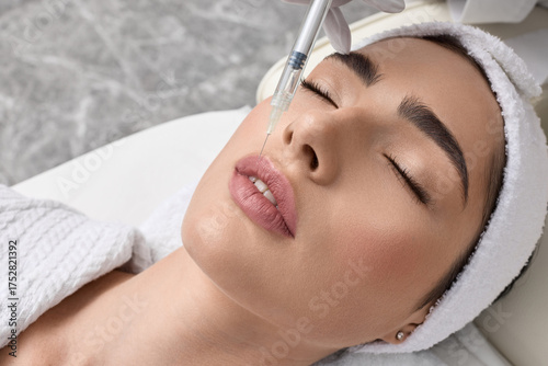 Lips filler injection for beautiful woman's lip augmentation with beautician on blue background. Lip augmentation procedure