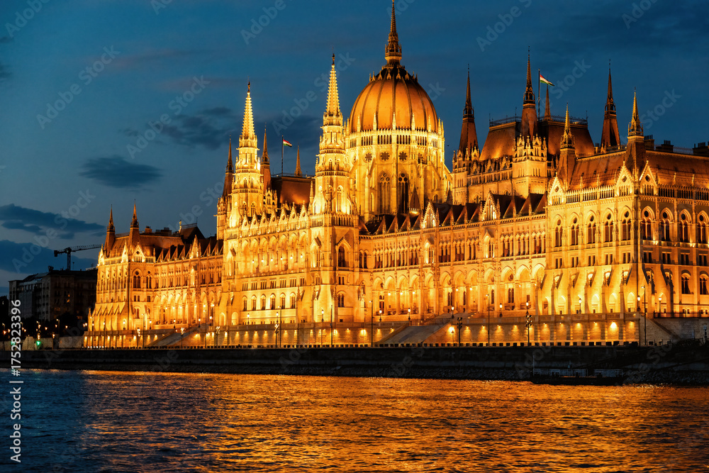 Fototapeta premium The Hungarian Parliament Building shines brilliantly at night, its golden lights reflected in the Danube River
