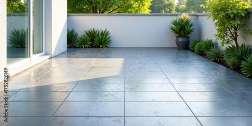 Serene outdoor patio with modern gray tiles, lush greenery, and bright sunlight reflecting off the smooth surface. © napak