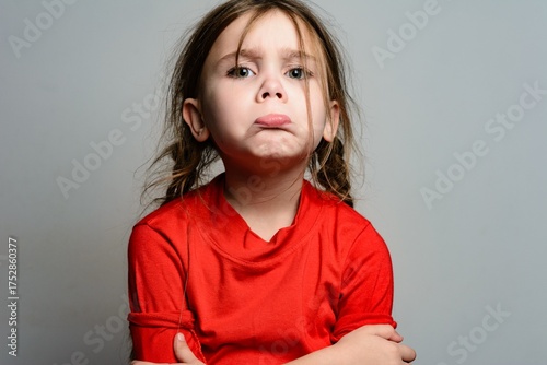 Upset young girl with arms crossed, wearing a red shirt. A portrait showing a child's emotional expression.