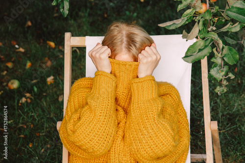 Woman hiding face in yellow sweater while resting outdoors in autumn