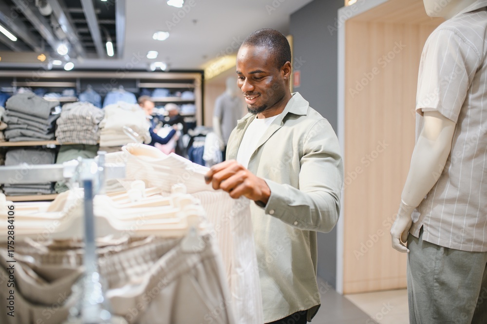 Fototapeta premium Smiling man choosing clothes in modern clothing store