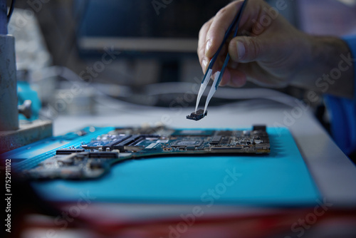 A technician works on a complex circuit board with precision tools and techniques
