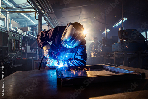 Industrial worker welding metal frame in factory workshop