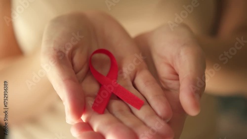 Female hands carefully unveiling red awareness ribbon on open palm, representing solidarity with HIV-positive individuals and December awareness month.