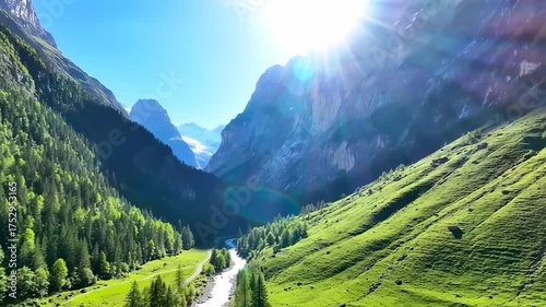Sunlight bathes a lush mountain valley with a river winding between green slopes and high peaks