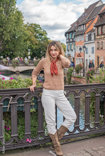 Woman wearing a beige knitted sweater, white jeans, and sunglasses, with a brown silk scarf. Casual chic outfit perfect for lifestyle, fashion on French street